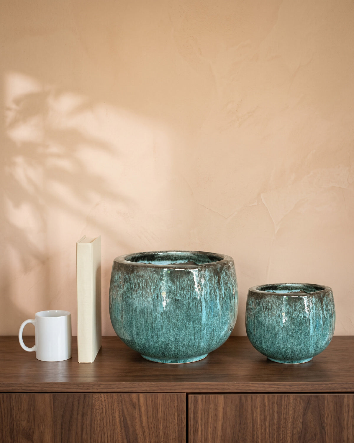 Aqua Glossy Pot, all sizes, shown on a walnut sideboard next to a coffee mug and a book for scale