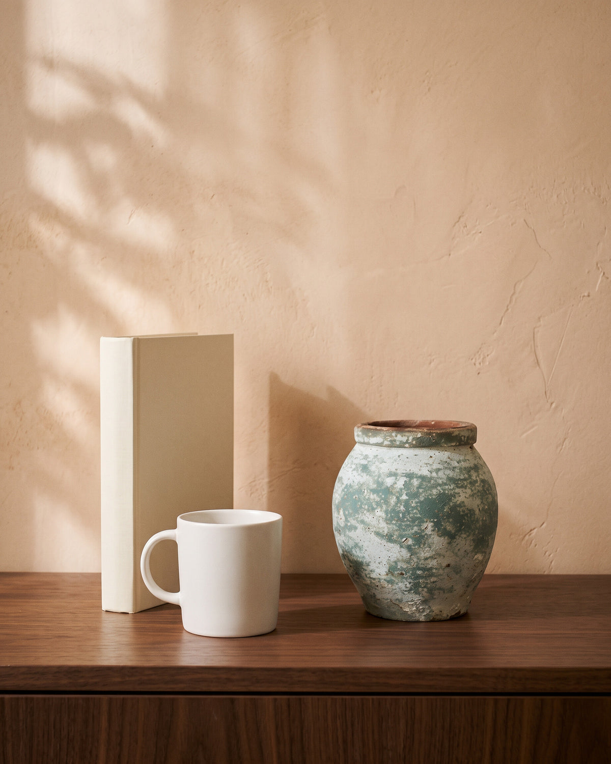 Moss Green Atlantic Vase, shown on a walnut sideboard next to a coffee mug and a book for scale