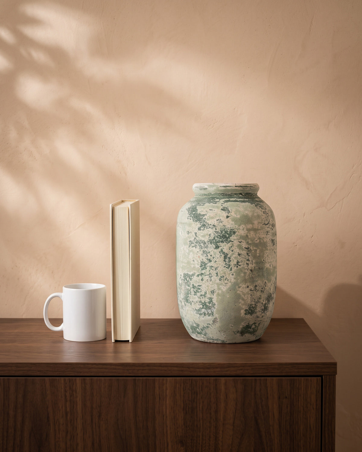 Atlantic Moss Green Cylindrical Vase, shown on a walnut sideboard next to a coffee mug and a book for scale