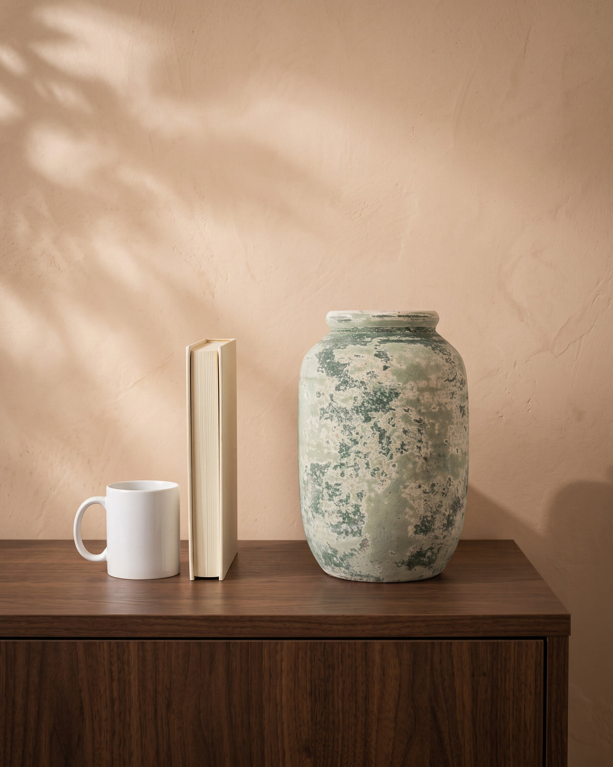 Atlantic Moss Green Cylindrical Vase, shown on a walnut sideboard next to a coffee mug and a book for scale