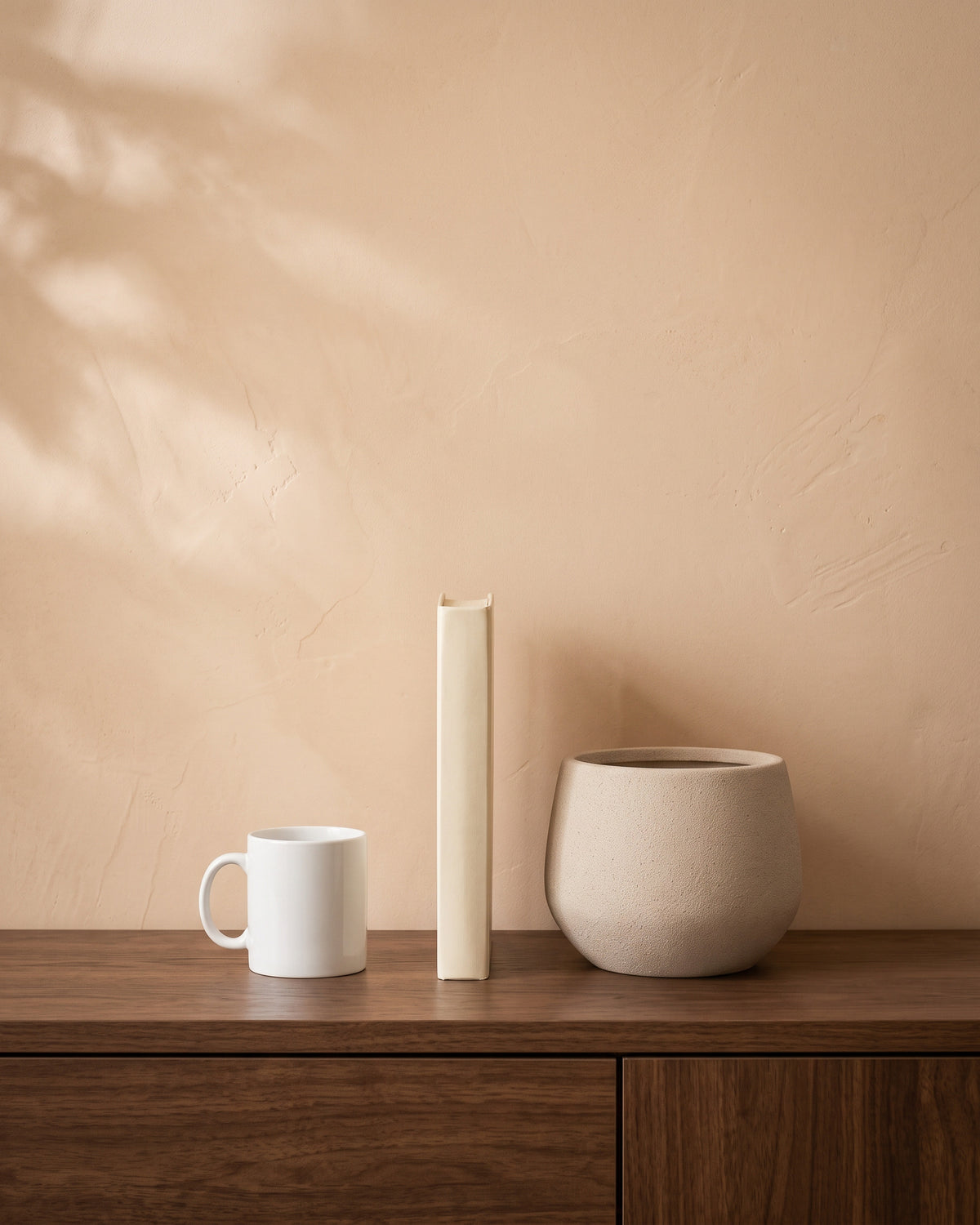 Sand Beige Round Pot, shown on a walnut sideboard next to a coffee mug and a book for scale