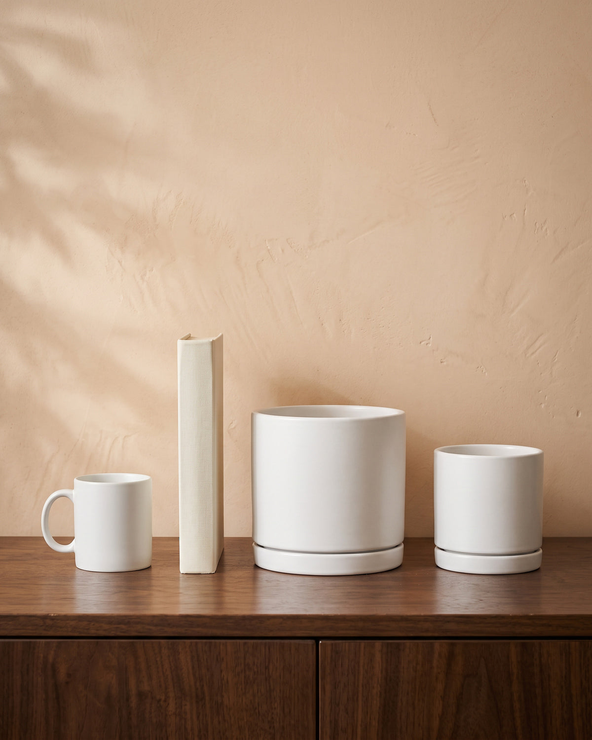 Matt White Pot, all sizes, shown on a walnut sideboard next to a coffee mug and a book for scale