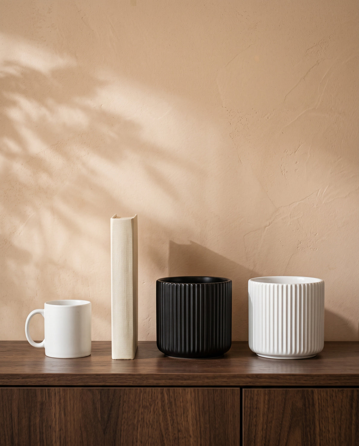 Linear Pot, in black and white, shown on a walnut sideboard next to a coffee mug and a book for scale