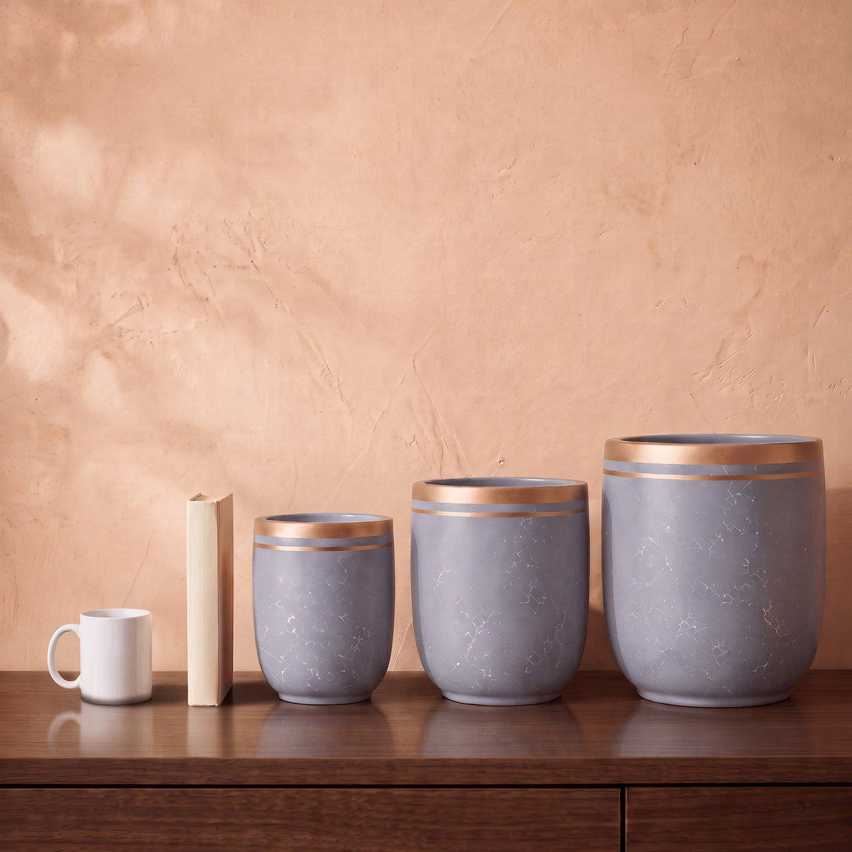 Marble Pot in grey, all sizes, shown on a walnut sideboard next to a coffee mug and a book for scale