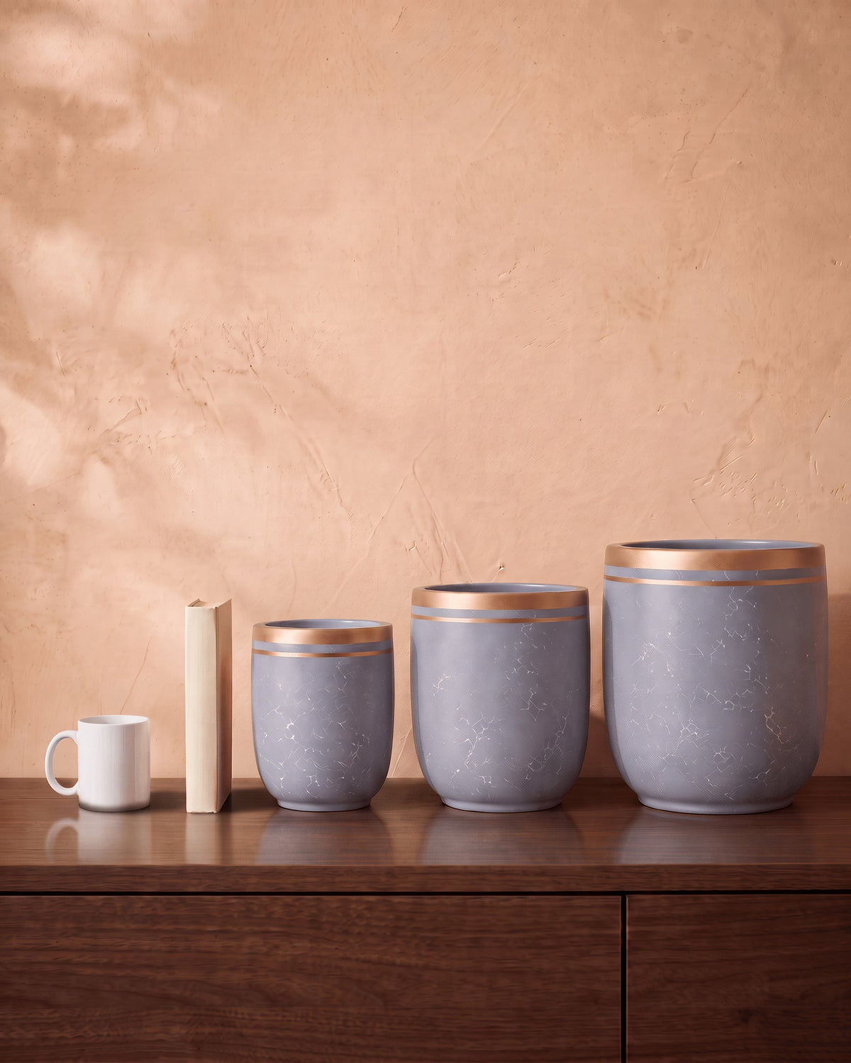 Marble Pot in grey, all sizes, shown on a walnut sideboard next to a coffee mug and a book for scale