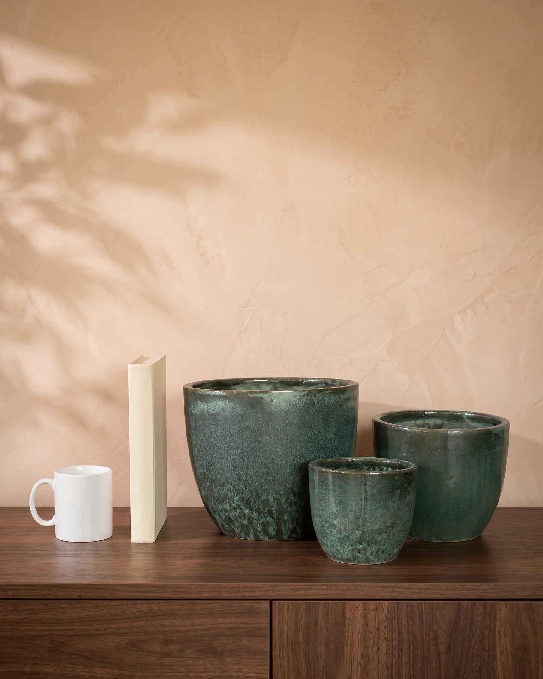 Moss Green Glazy Pot, all sizes, shown on a walnut sideboard next to a coffee mug and a book for scale