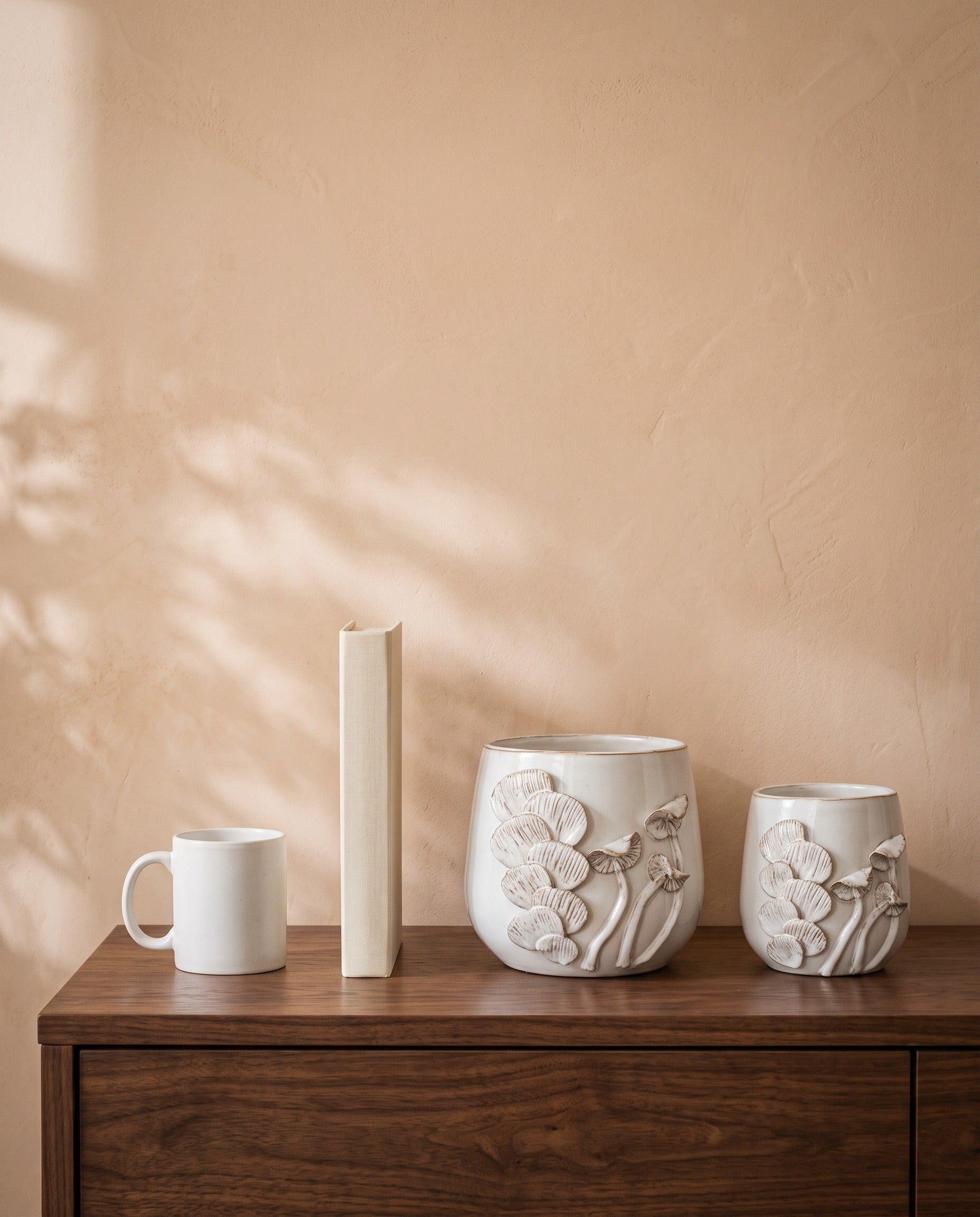 White Glossy Floral Pot, all sizes, shown on a walnut sideboard next to a coffee mug and a book for scale