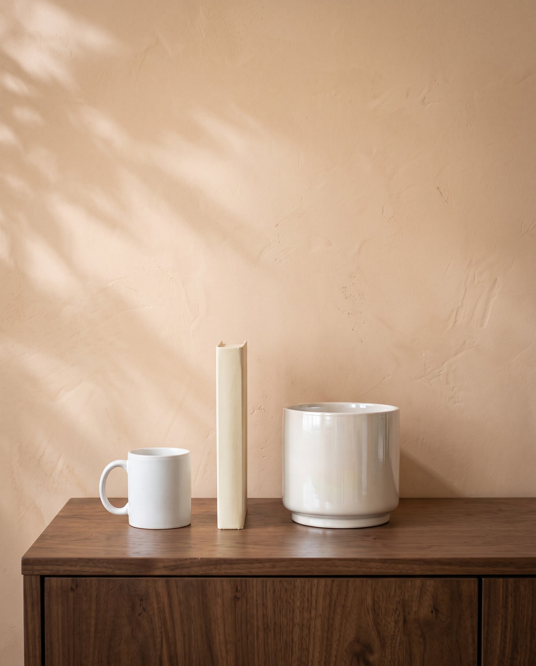 Pearl White Glossy Pot, shown on a walnut sideboard next to a coffee mug and a book for scale