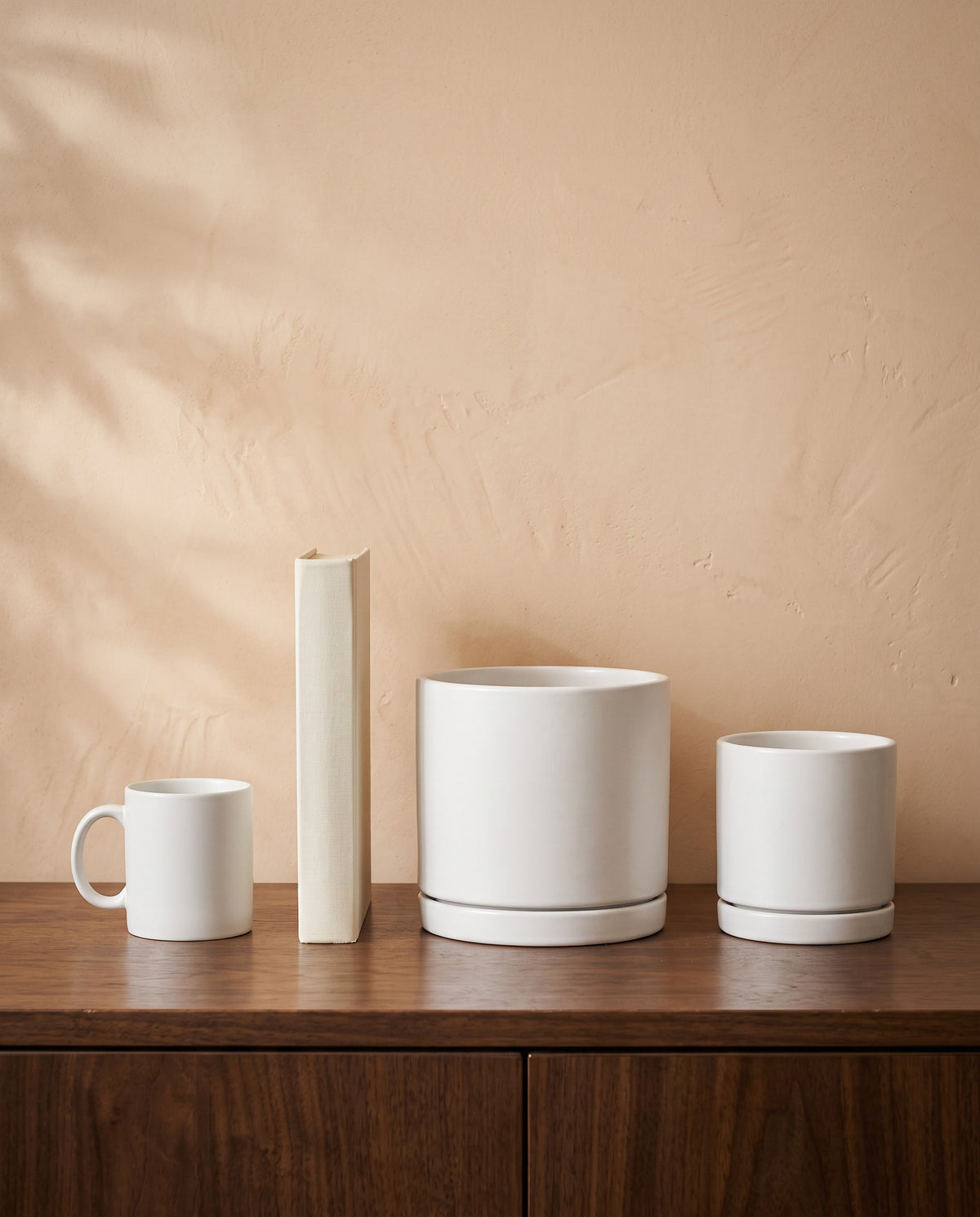 Matt White Pot, all sizes, shown on a walnut sideboard next to a coffee mug and a book for scale