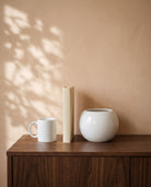 Glossy White Globe, shown on a walnut sideboard next to a coffee mug and a book for scale