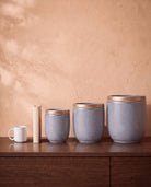 Marble Pot in grey, all sizes, shown on a walnut sideboard next to a coffee mug and a book for scale