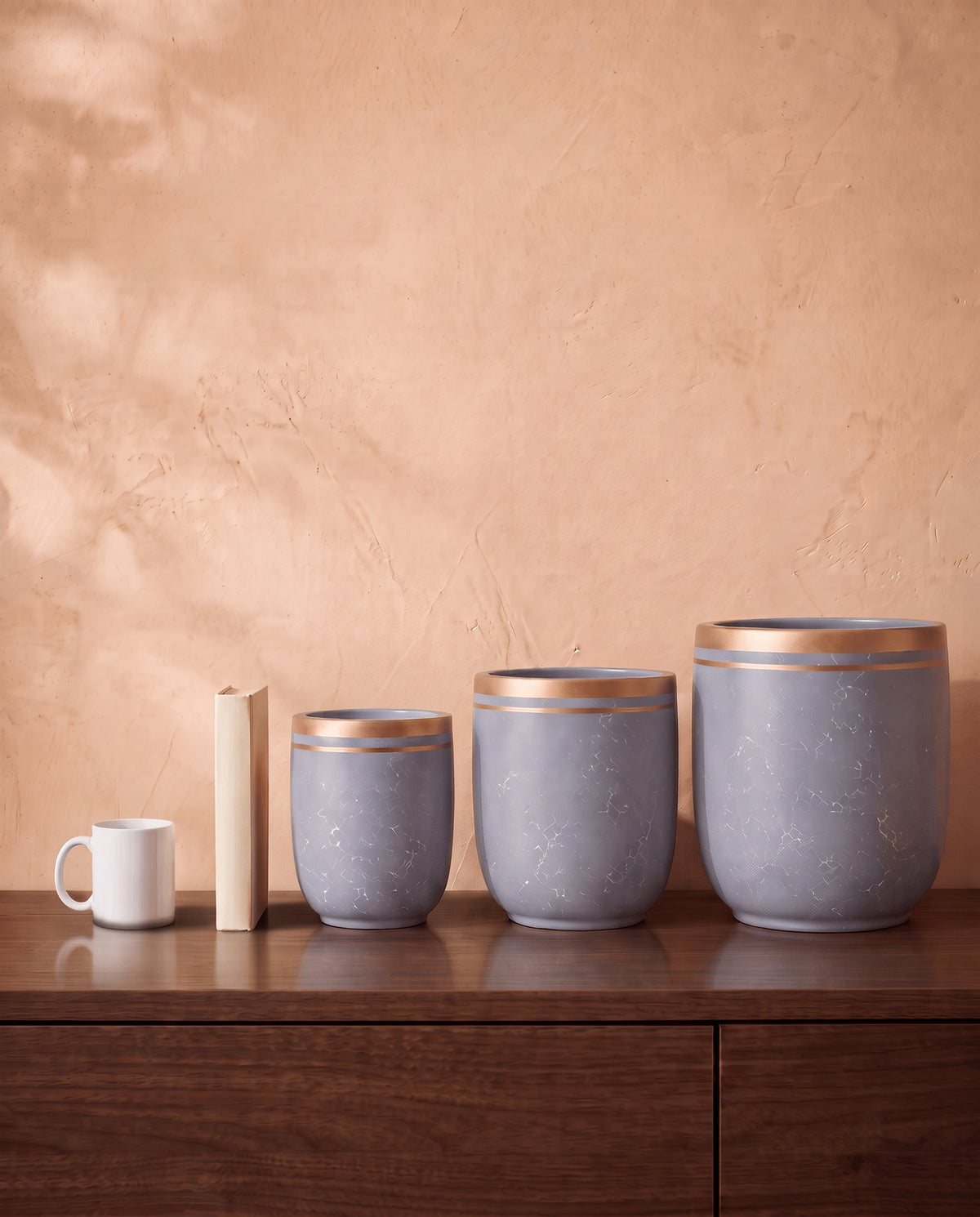 Marble Pot in grey, all sizes, shown on a walnut sideboard next to a coffee mug and a book for scale